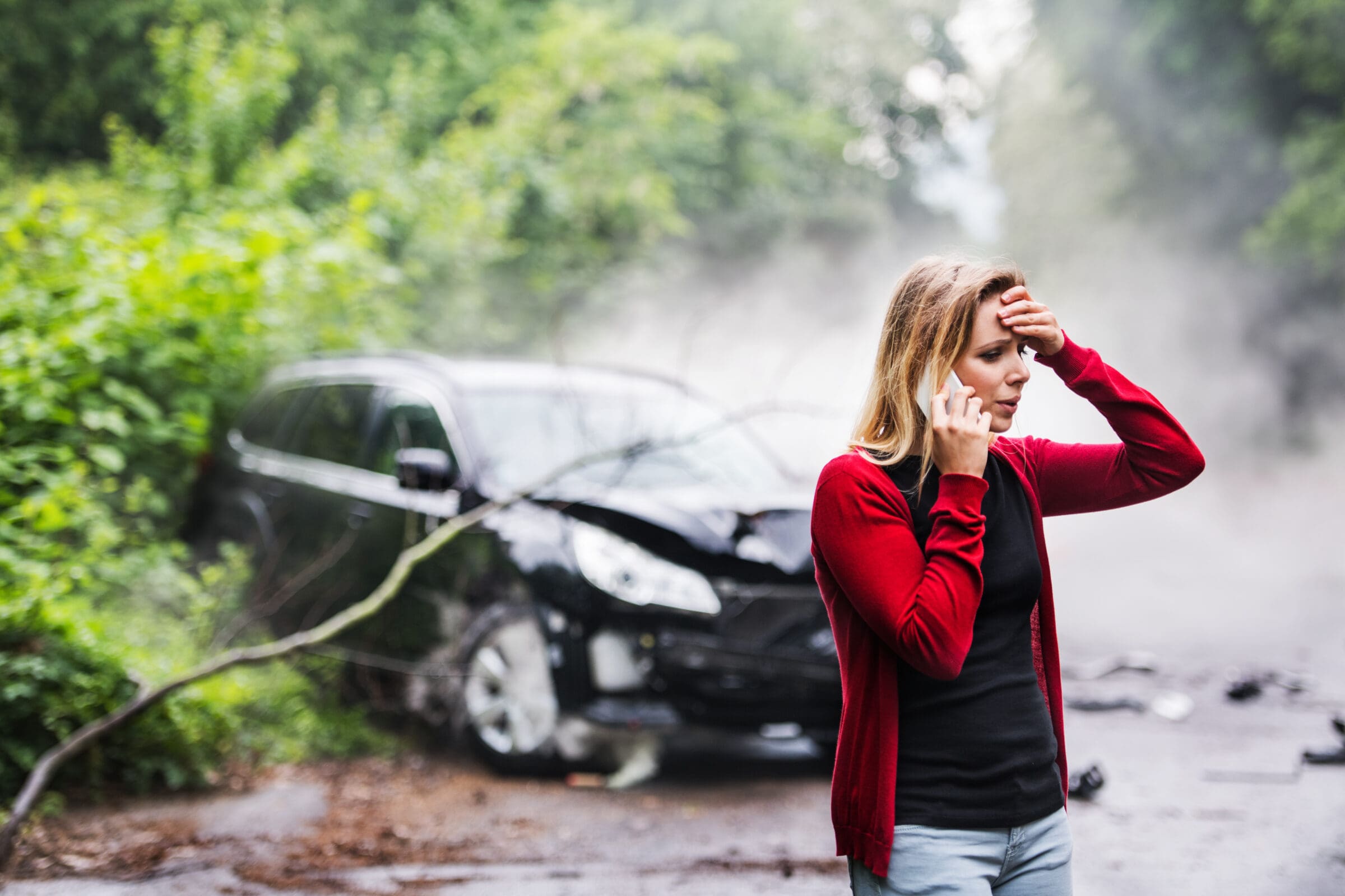 A young woman with smartphone by the damaged car after a car accident, making a phone call. A young woman with smartphone by the damaged car after a car accident, making a phone call.