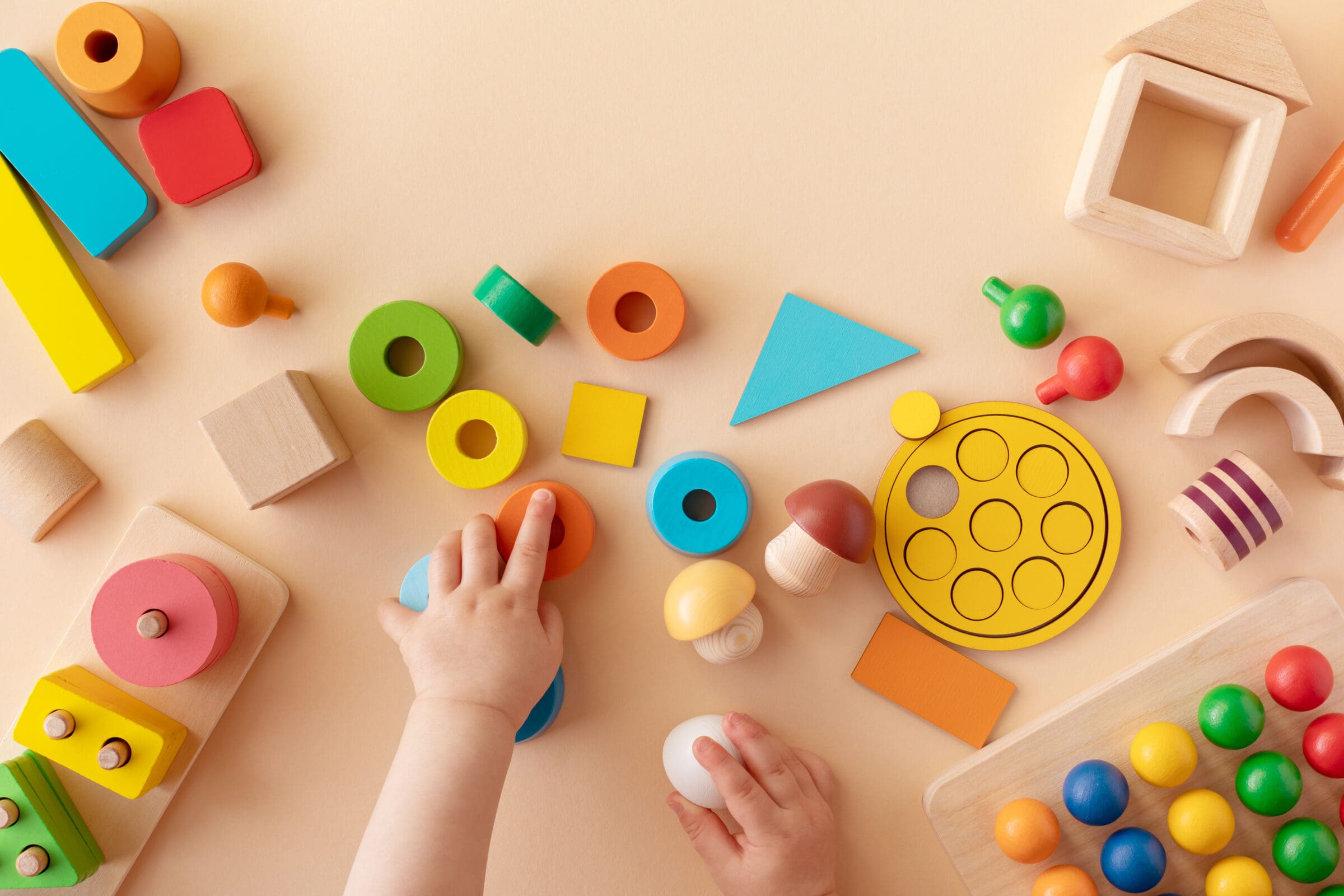 Toddler activity for motor and sensory development. Baby hands w Toddler activity for motor and sensory development. Baby hands with colorful wooden toys on table from above.